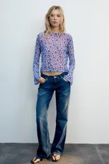 Top de punto fino color lila con estampado de flores abstractas en tonos azules y rojos, con cuello redondo y mangas largas acampanadas.