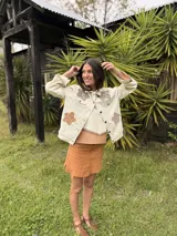 Campera de jean color off-white de corte trucker, con mangas largas y detalles de flores bordadas en crochet a tono en el frente.
