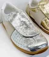 Zapatillas plateadas con detalles en cuero y gamuza color beige. Diseño con puntera perforada, cierre con velcro y suela de goma color caramelo.