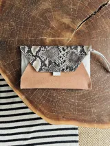 Sobre de cuero color naranja con estampado animal print, forrado y con bolsillo interior con cierre. Incluye pulsera desmontable.