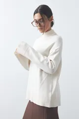 Polera de tejido liviano color negro con cuello alto y silueta relajada. Presenta mangas largas con puños ajustados y recortes laterales que aportan estructura al diseño.