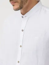 Camisa de manga larga confeccionada en lino orgánico, con cuello mao y cierre frontal de botones en tono madera. Presenta un diseño minimalista con bordado sutil al tono en el pecho.