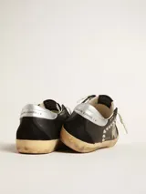 Zapatillas Golden Goose modelo Super-Star, confeccionadas en cuero negro con detalles en gamuza, estrella lateral gris y tachas metálicas plateadas. Cuentan con suela de goma con acabado envejecido y cordones de algodón crudo.