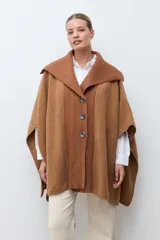 Capa de paño color marrón con cuello solapa y panel central de tejido acanalado. Cuenta con cierre frontal de tres botones grandes y diseño holgado.