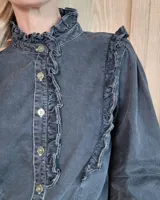 Camisa de denim negro con cuello alto, cierre frontal de botones y detalles de volados en el frente y puños.