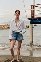 Shorts de jean tiro medio, corte mom fit, con bajo deshilachado y forro de bolsillos delanteros estampado a cuadros que asoma por debajo.