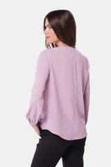 Blusa de manga larga con cuello redondo y cierre frontal parcial mediante botones forrados. Presenta diseño de doble capa en el frente y puños abotonados.