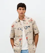 Camisa de corte relajado con cuello solapa y manga corta, confeccionada en algodón con estampa abstracta de palmeras y paisajes en tonos tierra, azul y rojo.