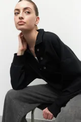 Buzo negro de algodón con cuello alto y apliques de argollas metálicas. De manga larga y corte holgado.