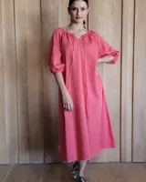 Vestido midi de corte holgado, color rosado, con escote en V y cordones ajustables. Presenta mangas tres cuartos abullonadas con puños elásticos.