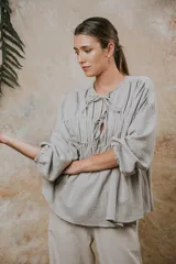 Camisa de algodón con textura arrugada, cuello redondo con cierre de cordones y mangas largas con puños elásticos. Presenta un diseño holgado con frunces en el pecho.