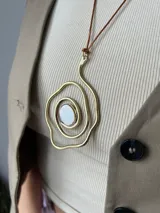 Collar con cordón marrón ajustable y dije dorado con forma de espiral irregular y centro de nácar.