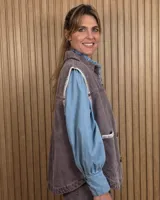 Chaleco de denim color marrón, confeccionado en 100% algodón, con bolsillos frontales amplios, cierre de botones y costuras decorativas bordadas en blanco en los bordes y los bolsillos.
