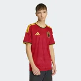 Camiseta de fútbol Adidas de la primera equipación de Bélgica, color rojo con patrón sutil de llamas y demonios. Presenta cuello redondo con ribete negro y amarillo, y detalles de las tres franjas amarillas en los hombros. El escudo de la RBFA está bordado en el pecho.