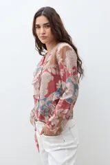 Blusa de manga larga con escote en V y volados en el frente. Presenta un estampado paisley en tonos rojo, azul y beige.