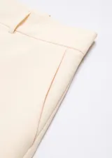 Pantalon de vestir de corte recto y tiro medio, confeccionado en tejido fluido color beige. Presenta trabillas en la cintura, dos bolsillos laterales y dos bolsillos de ribete en la parte posterior.