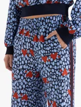Pantalón de corte relajado y fluido, confeccionado en viscosa estampada con diseño de corazones rojos sobre fondo azul con manchas oscuras. Presenta cintura elástica, bolsillos laterales y bandas laterales con vivos en contraste.