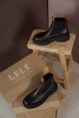 Botas tipo chelsea de cuero negro con textura granulada, paneles laterales elásticos y suela track robusta de goma.