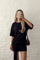 Vestido corto negro de ajuste entallado, con cuello redondo, mangas cortas y detalle de fruncido lateral con caída asimétrica.