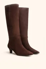 Bota de caña alta confeccionada en gamuza color marrón, con diseño minimalista, punta fina y taco kitten heel de 6 cm.