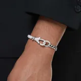 Pulsera plateada con una mitad de cadena de eslabones gruesos y la otra mitad de perlas blancas. El cierre es un mosquetón adornado con cristales transparentes.