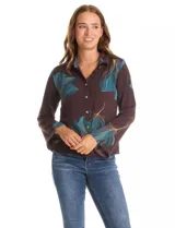 Camisa de crepe marca ABS Allen Schwartz, color marrón con estampado de hojas en tonos verdes y azules. Presenta cuello con solapa, cierre frontal con botones, mangas largas anchas y detalle de bordado con mostacillas en los hombros.