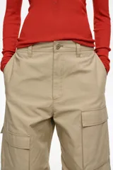Pantalón cargo beige de tiro bajo y corte ancho, con múltiples bolsillos con solapa en los laterales de las piernas y cierre frontal con botón y cremallera oculta.