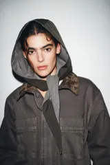 Capucha de diseño estructurado con exterior liso y forro interior con estampado de cuadros. Presenta un cierre frontal con lazada.