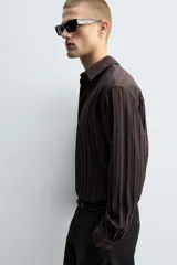 Camisa de manga larga con ajuste relajado, confeccionada en tejido de viscosa con textura de rayas verticales. Presenta cuello camisero, cierre frontal de botones y aberturas en el bajo lateral.