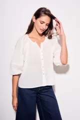 Blusa blanca de algodón peinado, con escote redondo y abertura frontal con botones. Presenta mangas globo de tres cuartos con elástico en el puño y corte holgado.