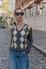 Chaqueta de punto con cuello en pico y manga larga. Presenta un diseño de estampado de rombos en tonos gris, beige y blanco en la parte frontal y cierre frontal con botones.