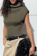 Top de tejido de punto acanalado color verde militar, con cuello alto tipo tortuga y mangas sisa. Presenta un bajo asimétrico con aberturas laterales.