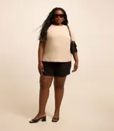 Blusa de manga corta color beige, confeccionada en tela texturizada. Presenta cuello redondo con detalle de pespuntes y cierre trasero con botón en forma de lágrima.