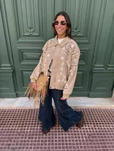 Campera tipo bomber de gamuza color beige, con diseño bordado de flores y motivos geométricos en blanco y negro. Presenta cuello clásico, cierre frontal con botones a presión y puños y ruedo de tejido elástico acanalado.