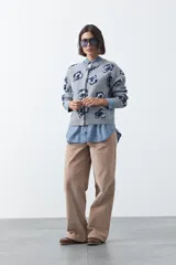 Cardigan de tejido jacquard color marrón con estampado floral en tonos rojo y rosado. Presenta cuello redondo, cierre frontal con botones y terminaciones acanaladas en puños y ruedo.