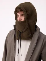 Pasamontañas de tejido tipo corderito en color verde oliva, con capucha integrada y cordón de ajuste frontal. Incluye etiqueta de la marca Rusty en el lateral.