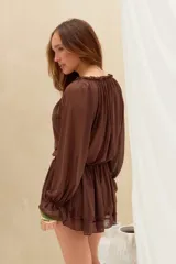 Vestido corto marrón de tejido semitransparente, con mangas largas abullonadas, escote redondo con cordones para ajustar y falda con volados en capas.
