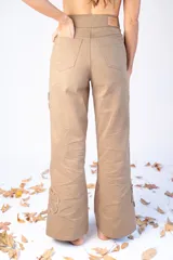 Pantalón largo color beige con parches en forma de flor con bordes desflecados.