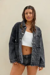 Campera de jean oversize en color negro con efecto acid wash, de mangas largas, cuello camisero, bolsillos frontales con solapa y cierre mediante botones metálicos.