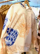 Buzo oversize de corte amplio con capucha, cordón de ajuste y aberturas en los costados del ruedo. Presenta una estampa multicolor con motivos de animales y flores.