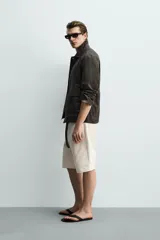 Sobrecamisa relaxed fit confeccionada en tejido de lino de color negro, con cuello solapa, manga larga con puño abotonado, bolsillos de plastrón en la cadera y cierre frontal de botones.