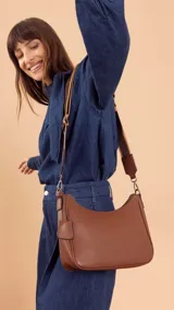 Bandolera de cuero sintético color marrón, con cierre trasero y división interna. Incluye correa de galón ajustable y un pequeño charm colgante.