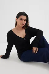 Sweater negro de tejido de punto acanalado, con escote en V y cierre frontal con cremallera circular.