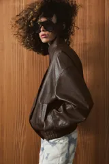 Chaqueta bomber de efecto piel en color marrón oscuro, con cuello subido, cierre frontal cruzado con botones a presión, bolsillos laterales y bajo elástico.