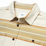 Camisa de franela a rayas horizontales en tonos beige, marrón y blanco, con cuello clásico, cierre frontal con botones y dos bolsillos con solapa en el pecho.