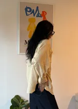 Camisa oversize de corte amplio con estampado de rayas verticales finas en tonos amarillo y azul. Presenta cuello clásico, cierre frontal con botones, mangas largas con puños abotonados y un bolsillo en el pecho.