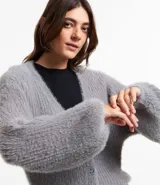 Cárdigan corto de punto color gris, con escote en V, cierre frontal con botones y mangas largas abullonadas.