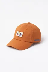 Gorra de lona color naranja con parche frontal bordado y la palabra Pastiche bordada en el lateral en color azul. Cuenta con diseño regulable en la parte posterior.