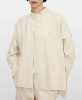 Sobrecamisa de efecto piel color beige, de corte recto y holgado, con cuello mao, manga larga, cierre frontal de botones y un bolsillo aplicado en el pecho.