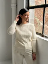 Sweater de punto color crudo con diseño de trenzas verticales, cuello redondo y mangas largas.